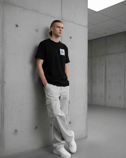 Person wearing a black t-shirt and white pants leaning against a concrete wall.